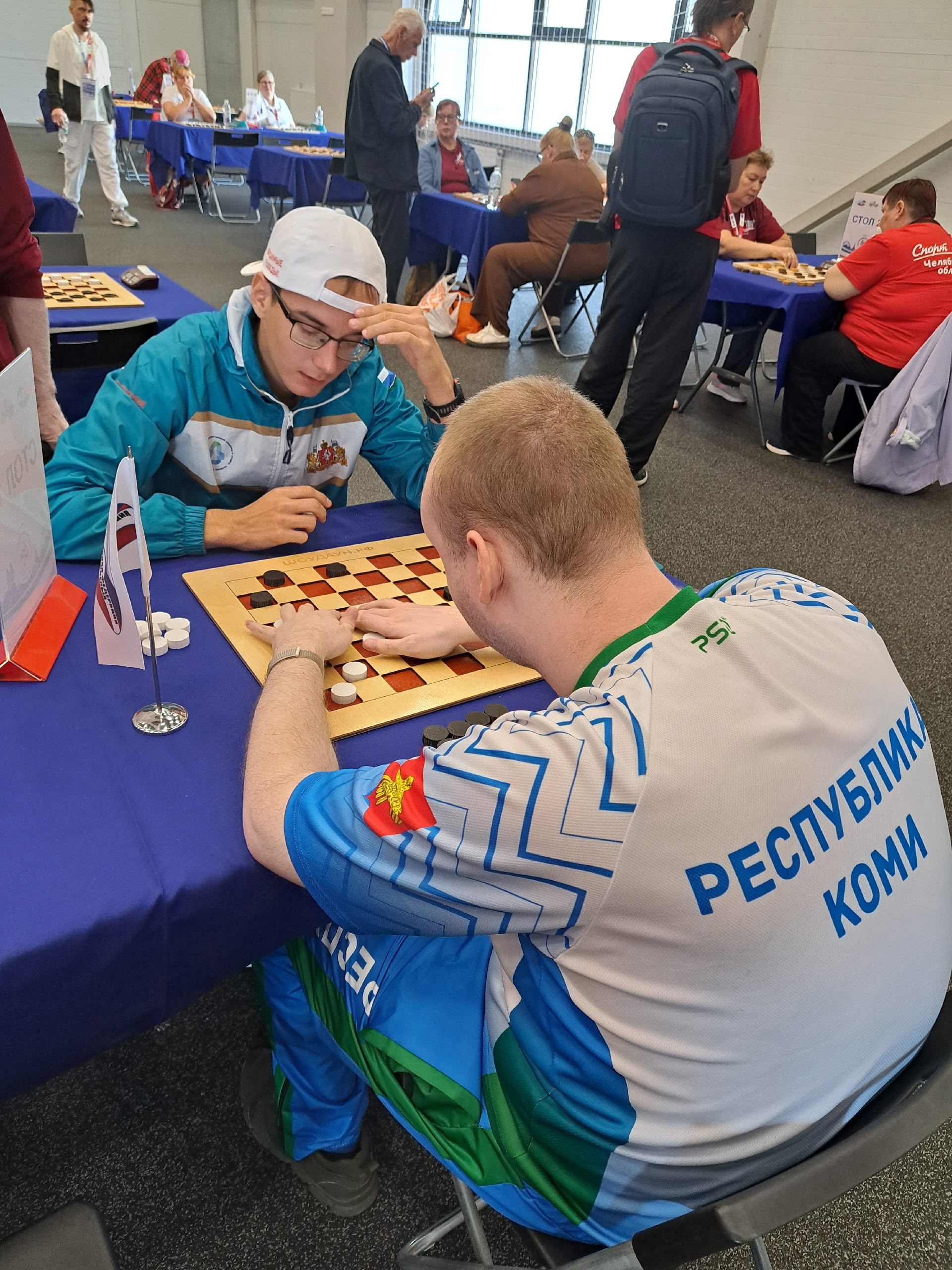Мужчина в спортивной форме Республики Коми играет в шашки с соперником в белой кепке