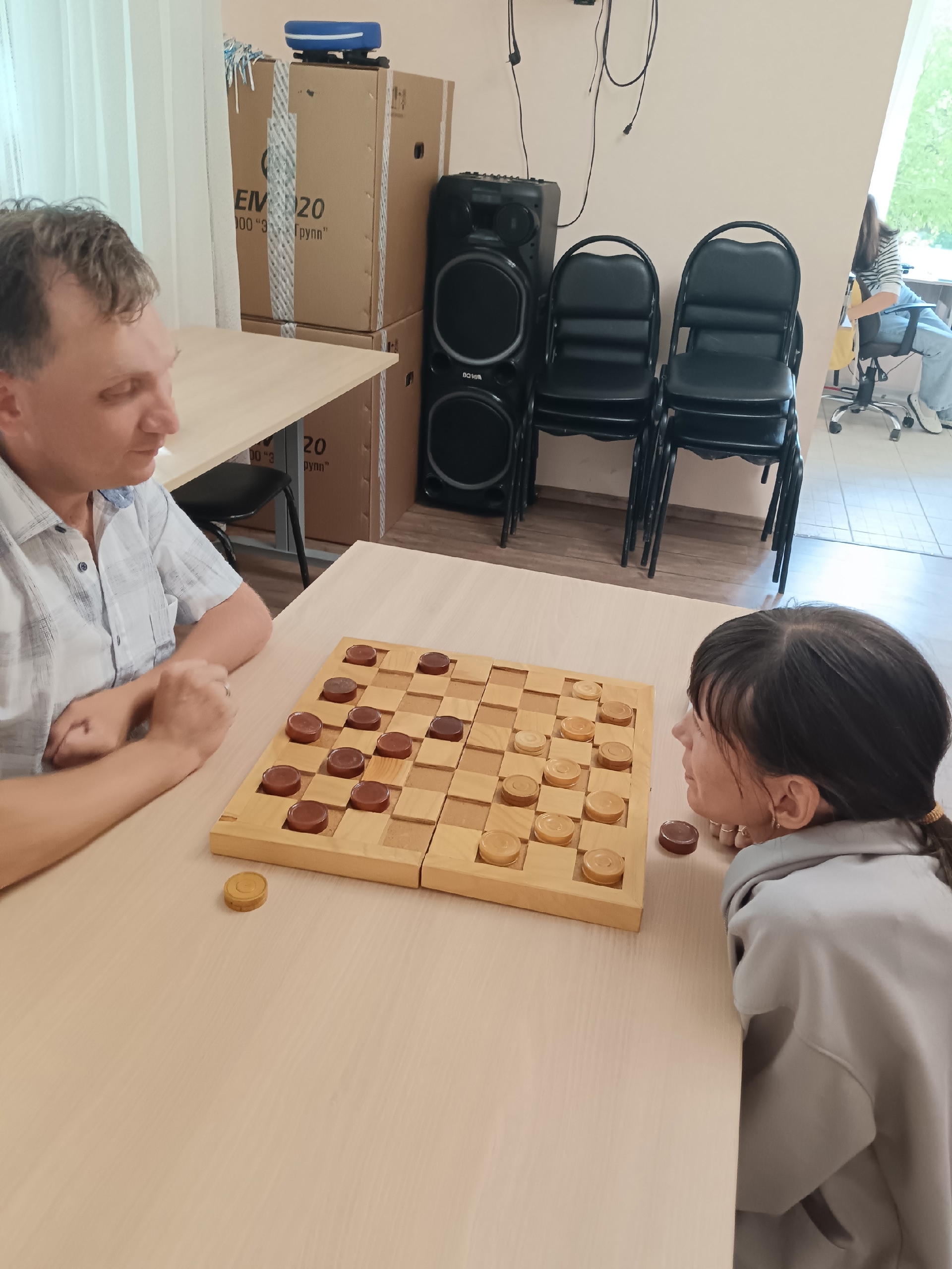 Мужчина и молодая девушка играют в шашки за деревянным столом