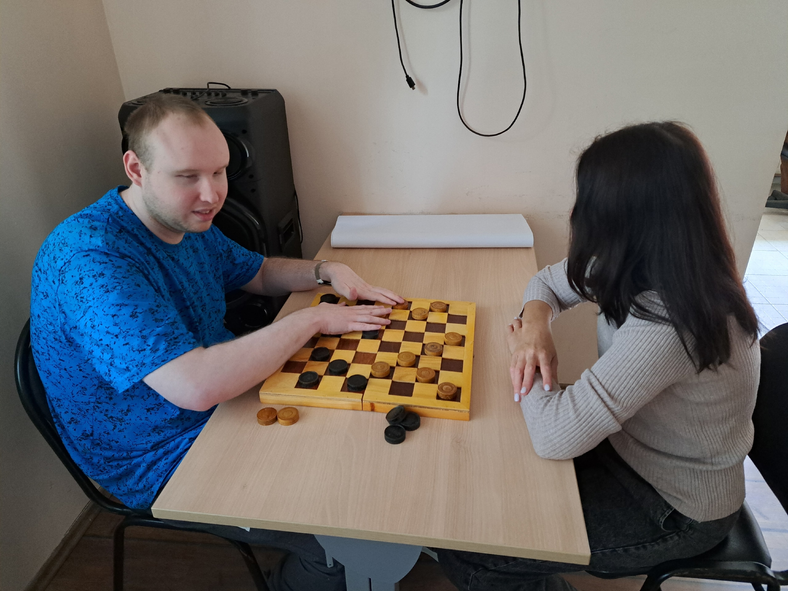 Мужчина в синей футболке и женщина сидят за столом и играют в шашки