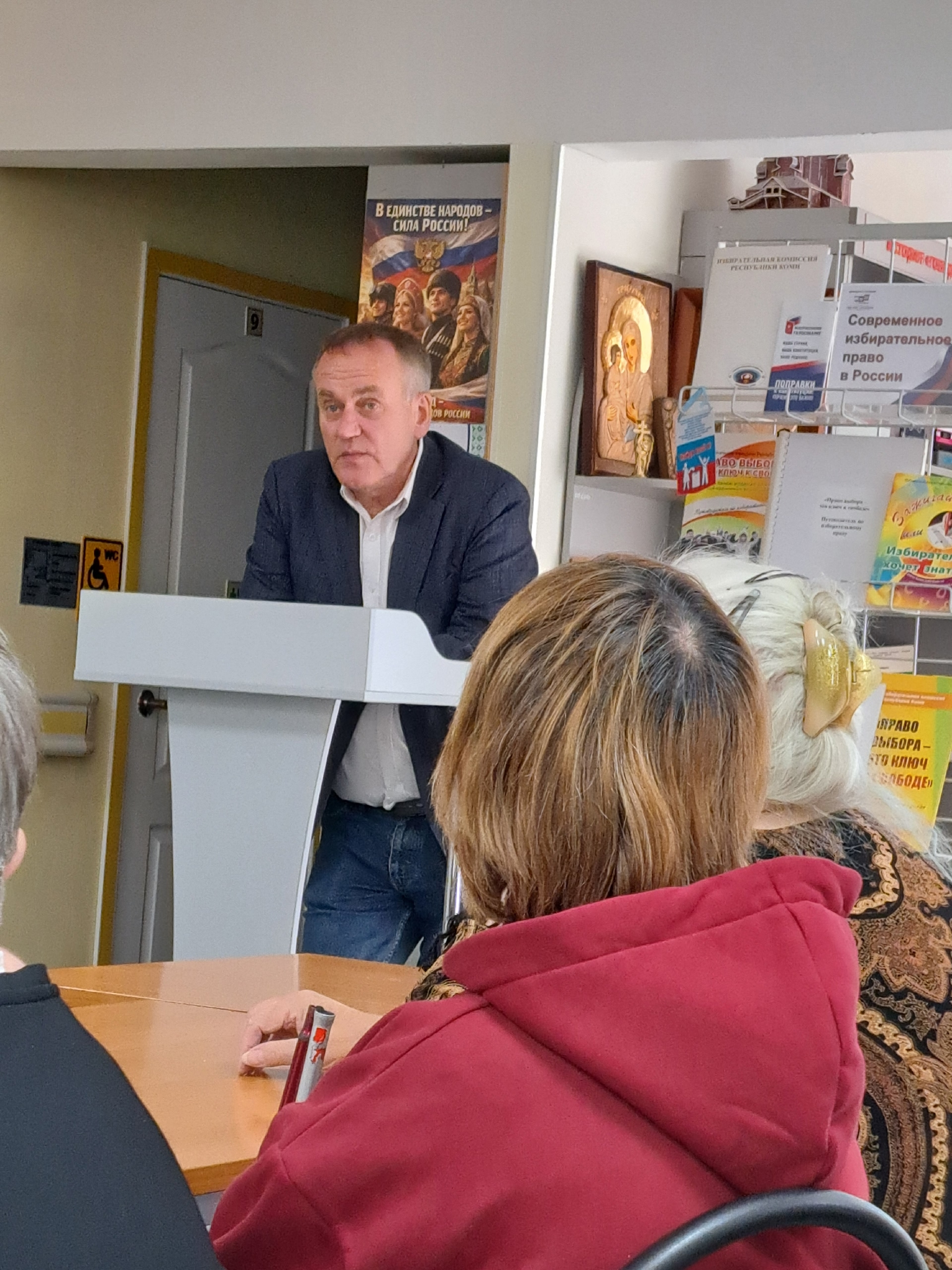 Мужчина выступает за трибуной перед слушателями в библиотеке