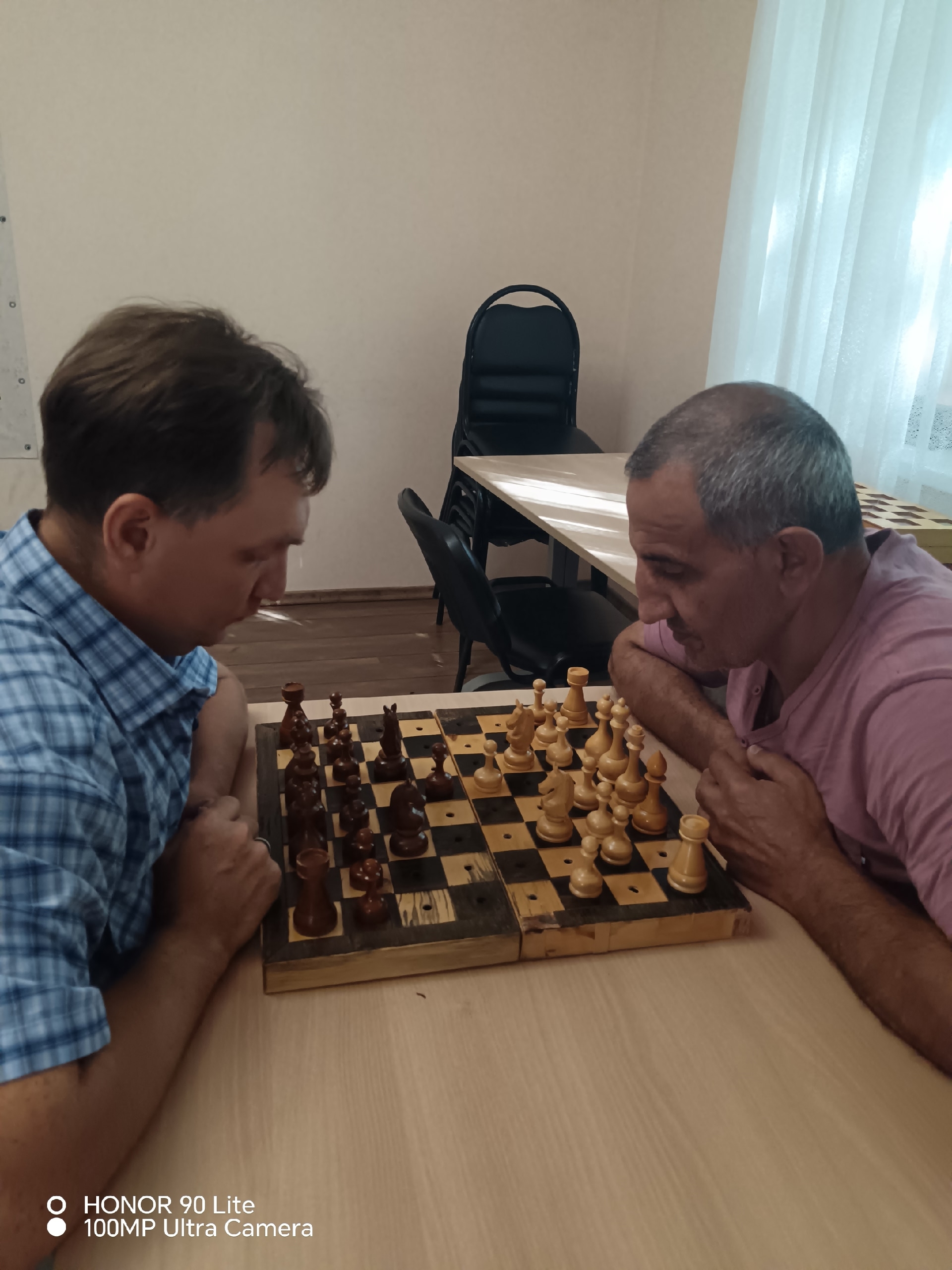 Двое мужчин сосредоточенно играют в шахматы за деревянным столом