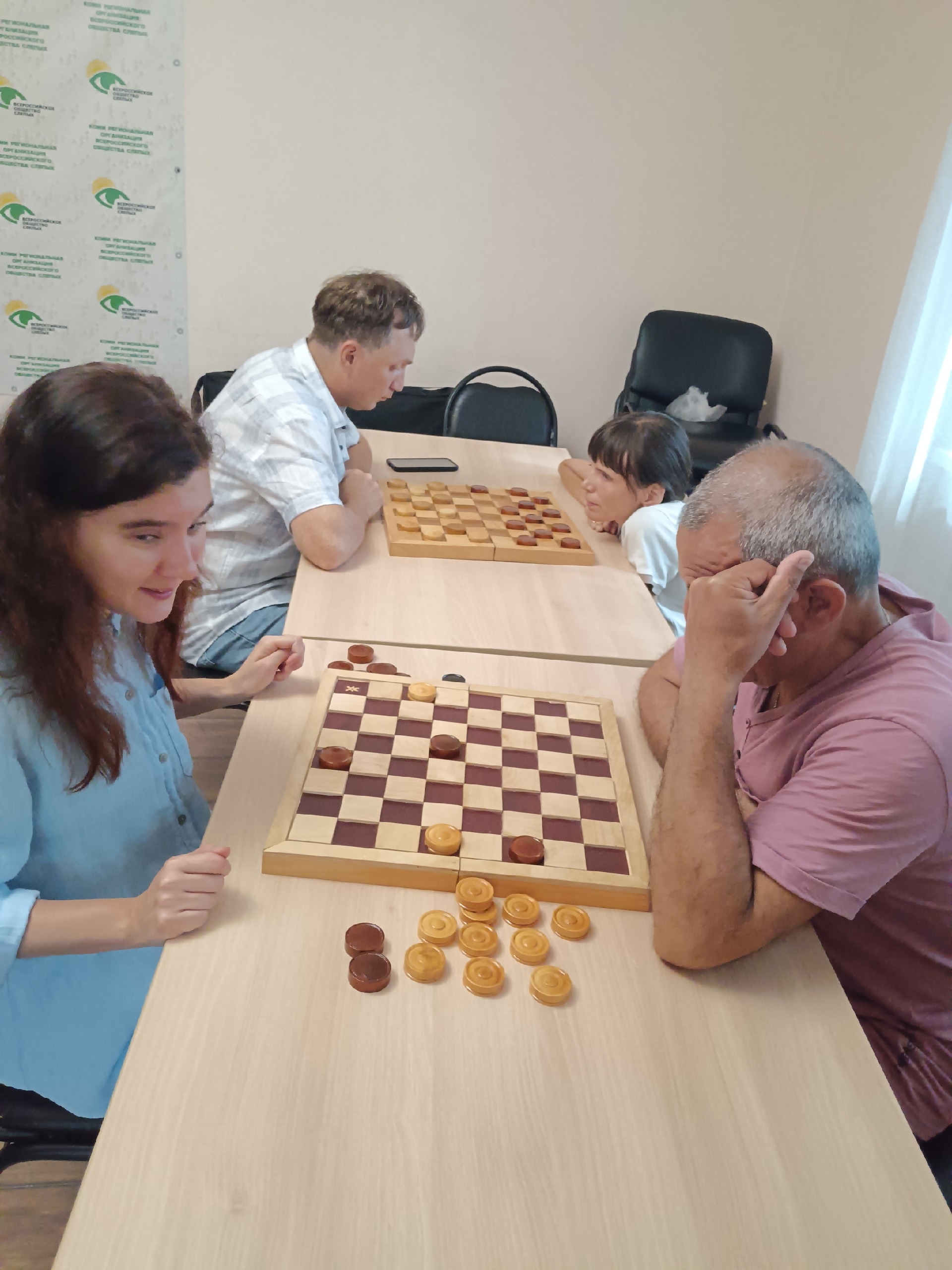 Женщина в голубой рубашке и мужчина в розовой футболке играют в шашки