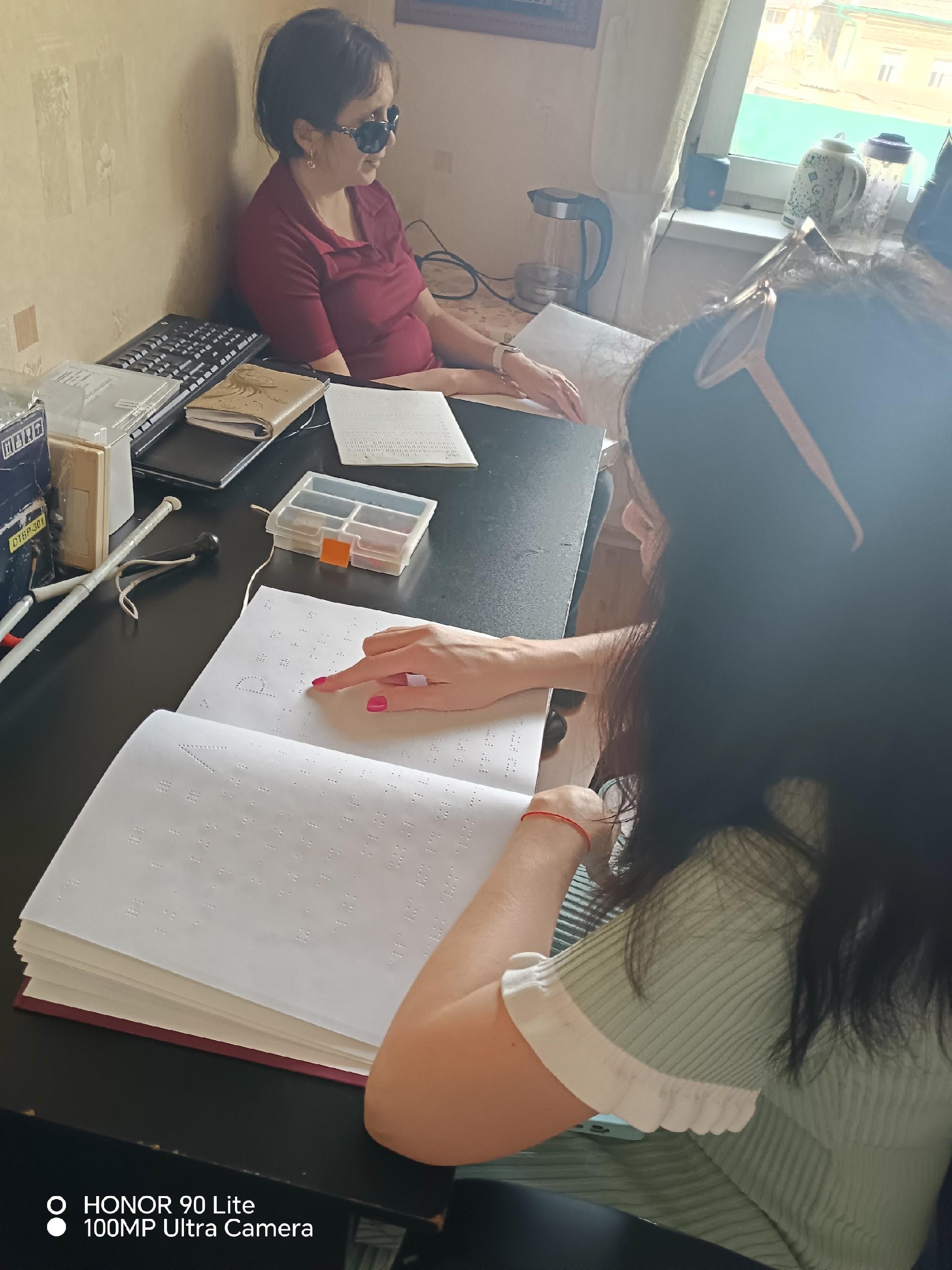 Женщина указывает пальцем на рельефные точки шрифта Брайля в открытой книге