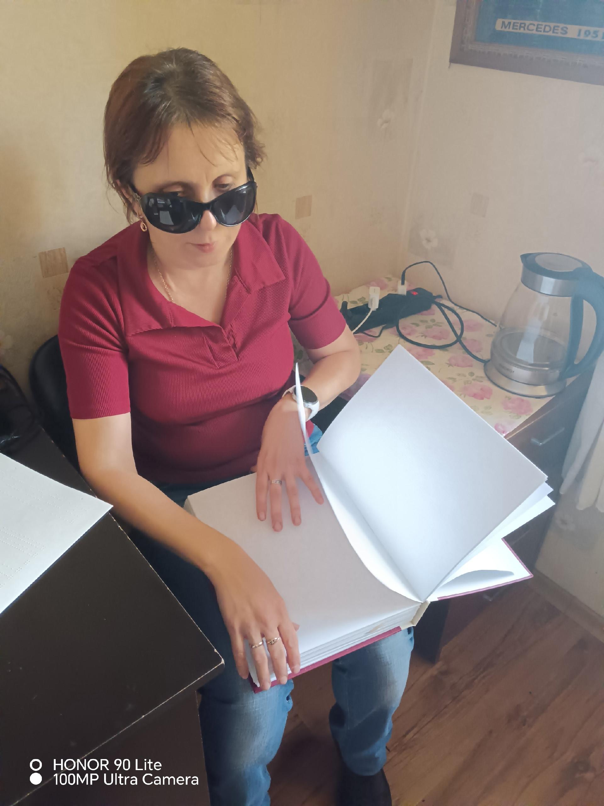 Женщина в темных очках держит открытую книгу со шрифтом Брайля