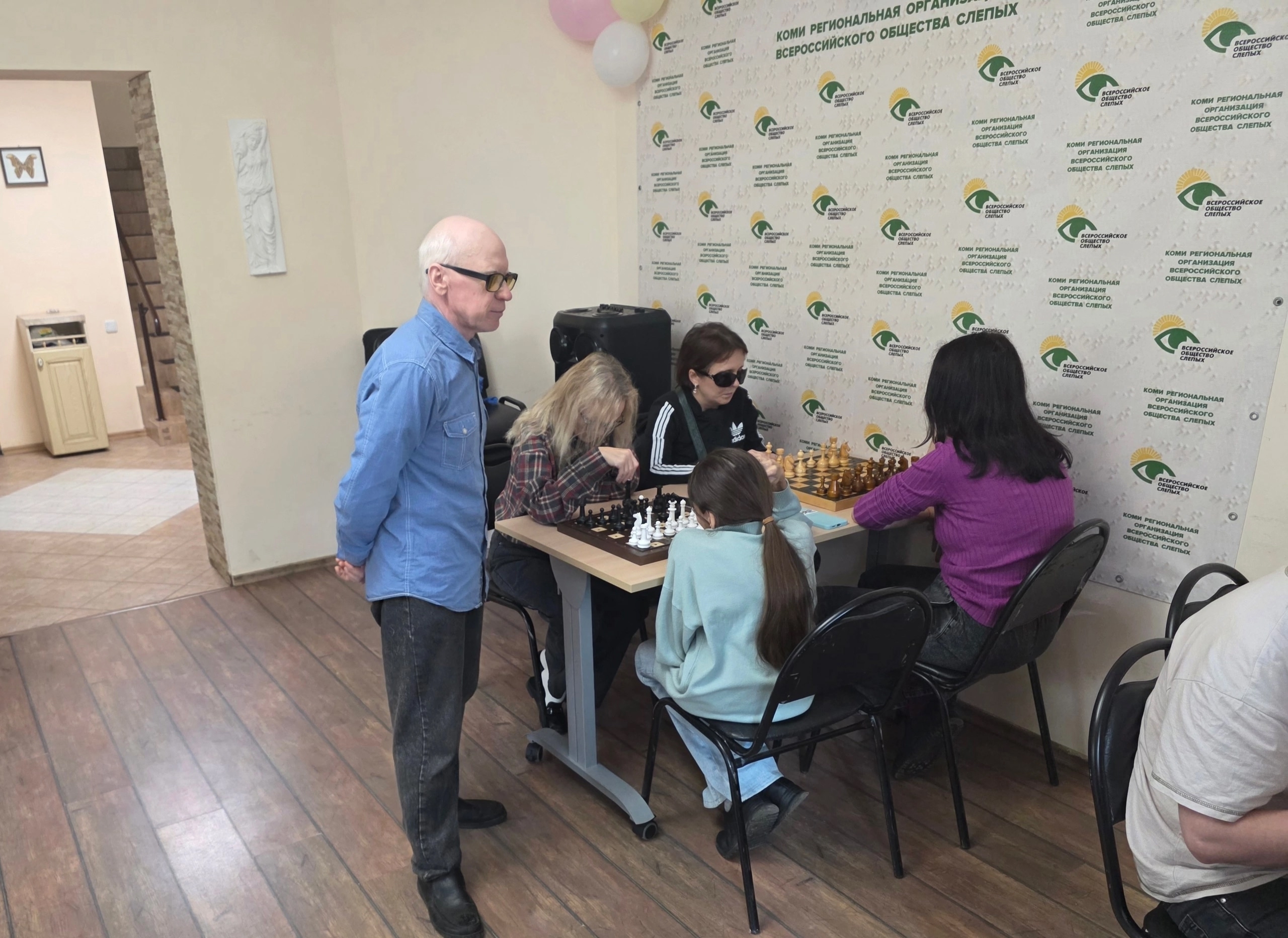 Преподаватель шахмат стоит рядом с участниками занятия во время игры