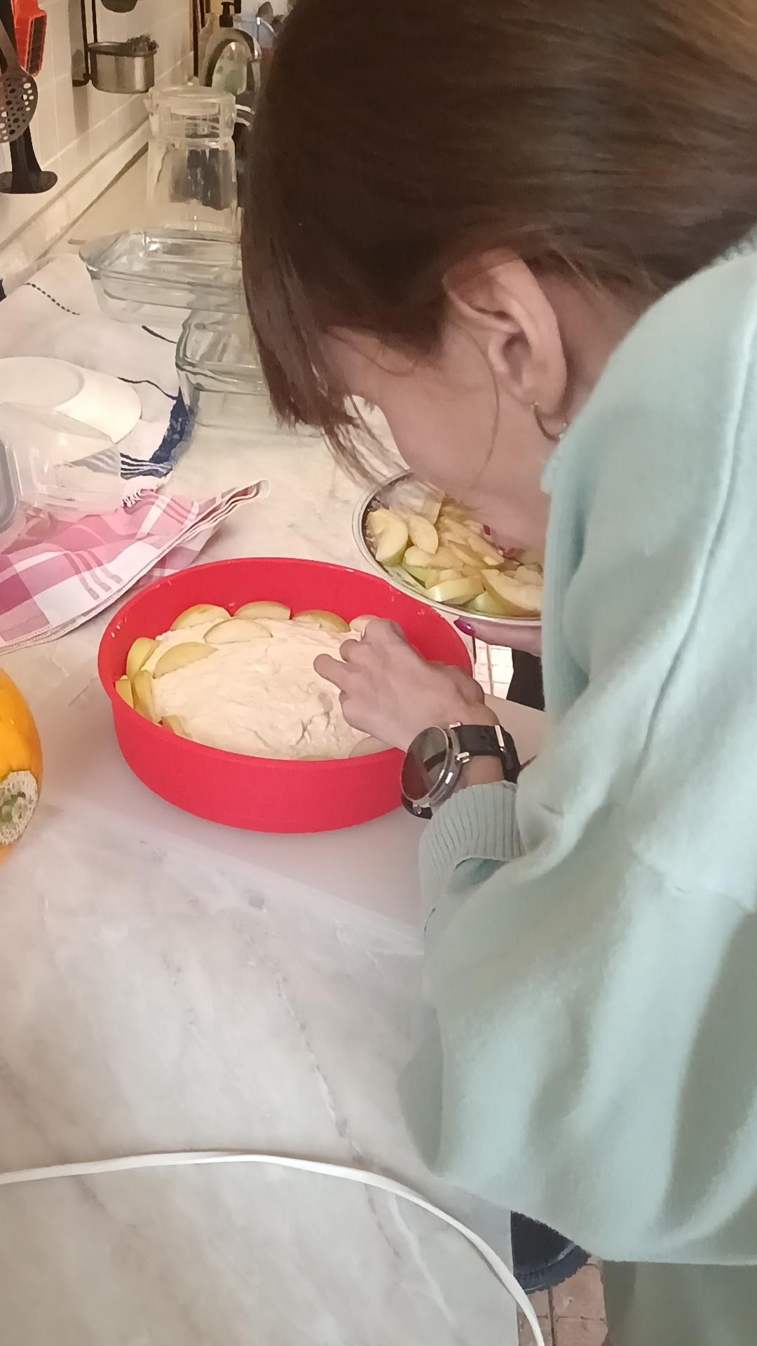 Женщина украшает тестом и яблоками заготовку пирога