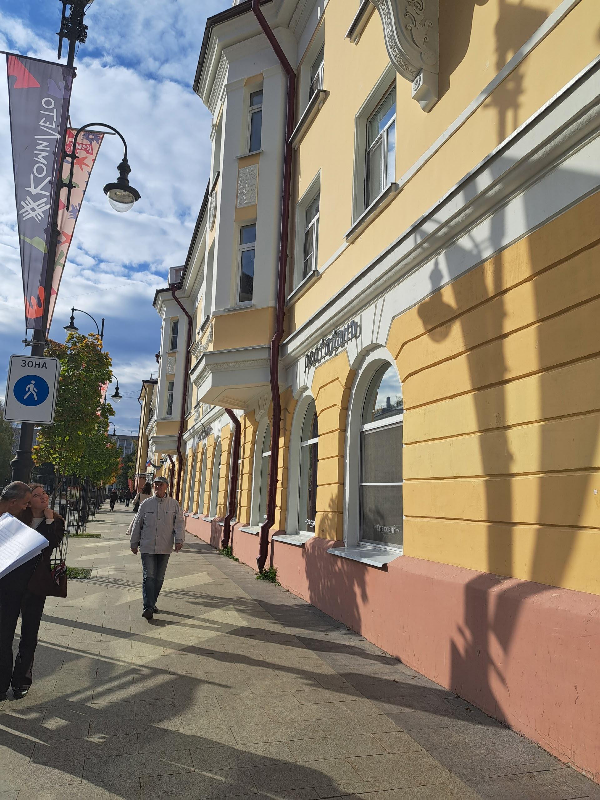 Прохожие на солнечном тротуаре возле старинного здания