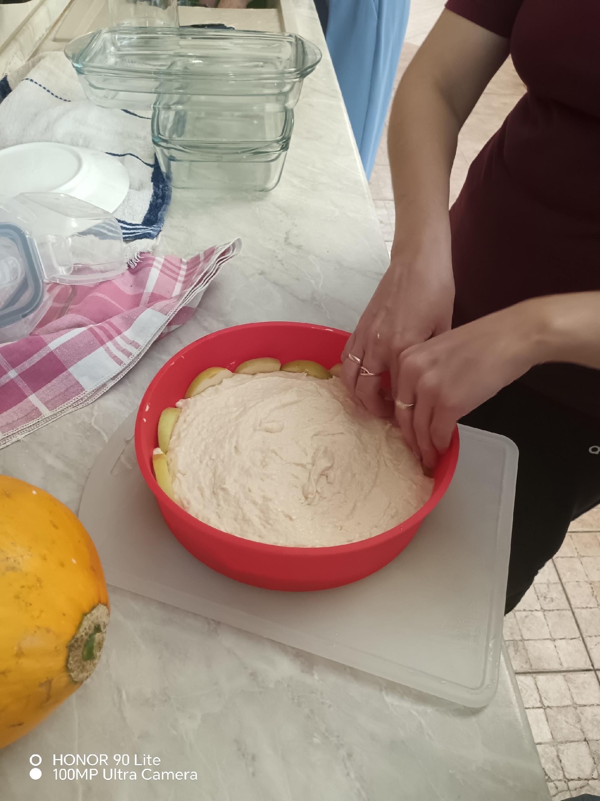 Женщина выкладывает нарезанные яблоки в форму для выпечки с тестом