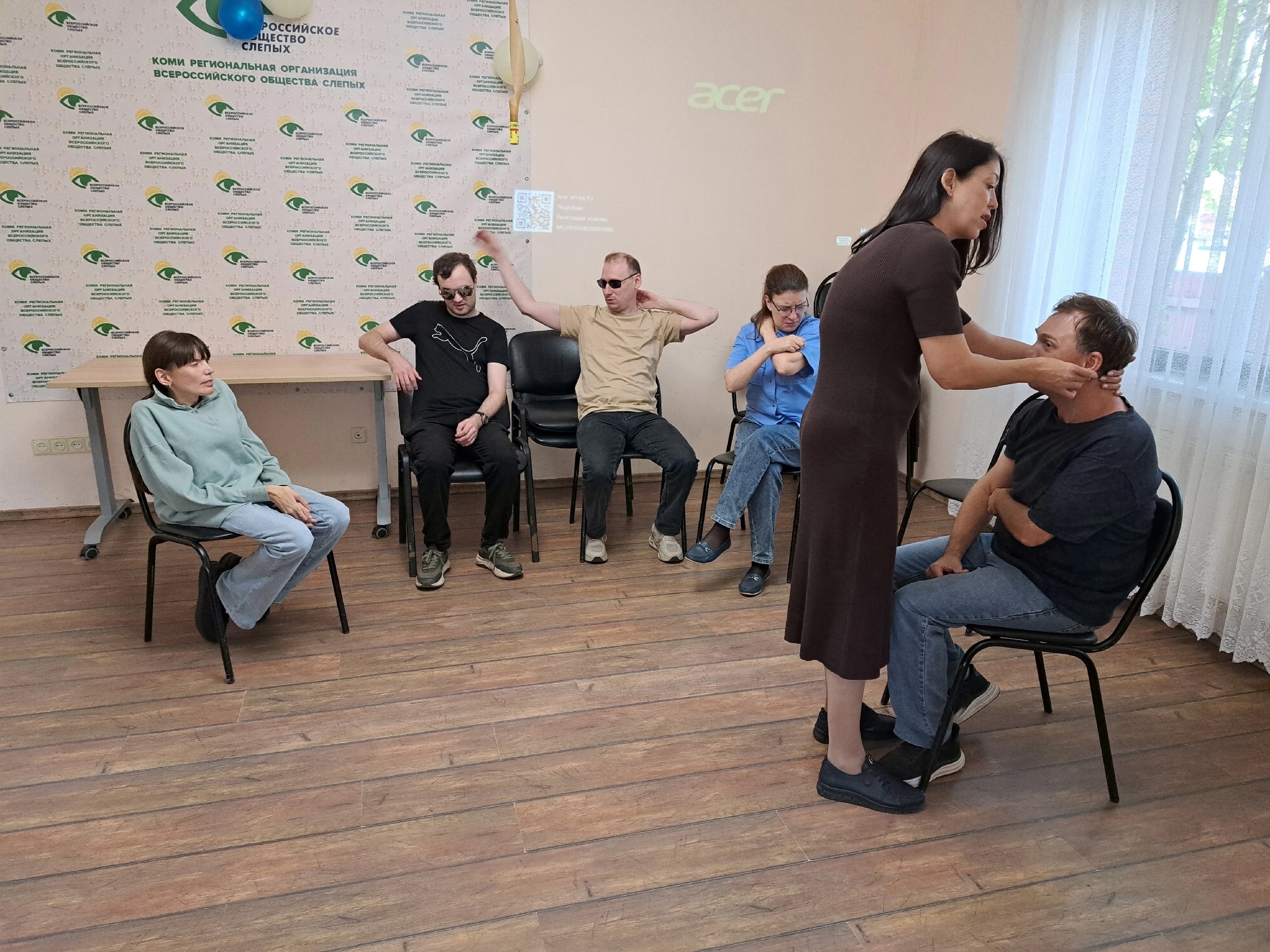 Участники занятия сидят на стульях и практикуют самомассаж шеи