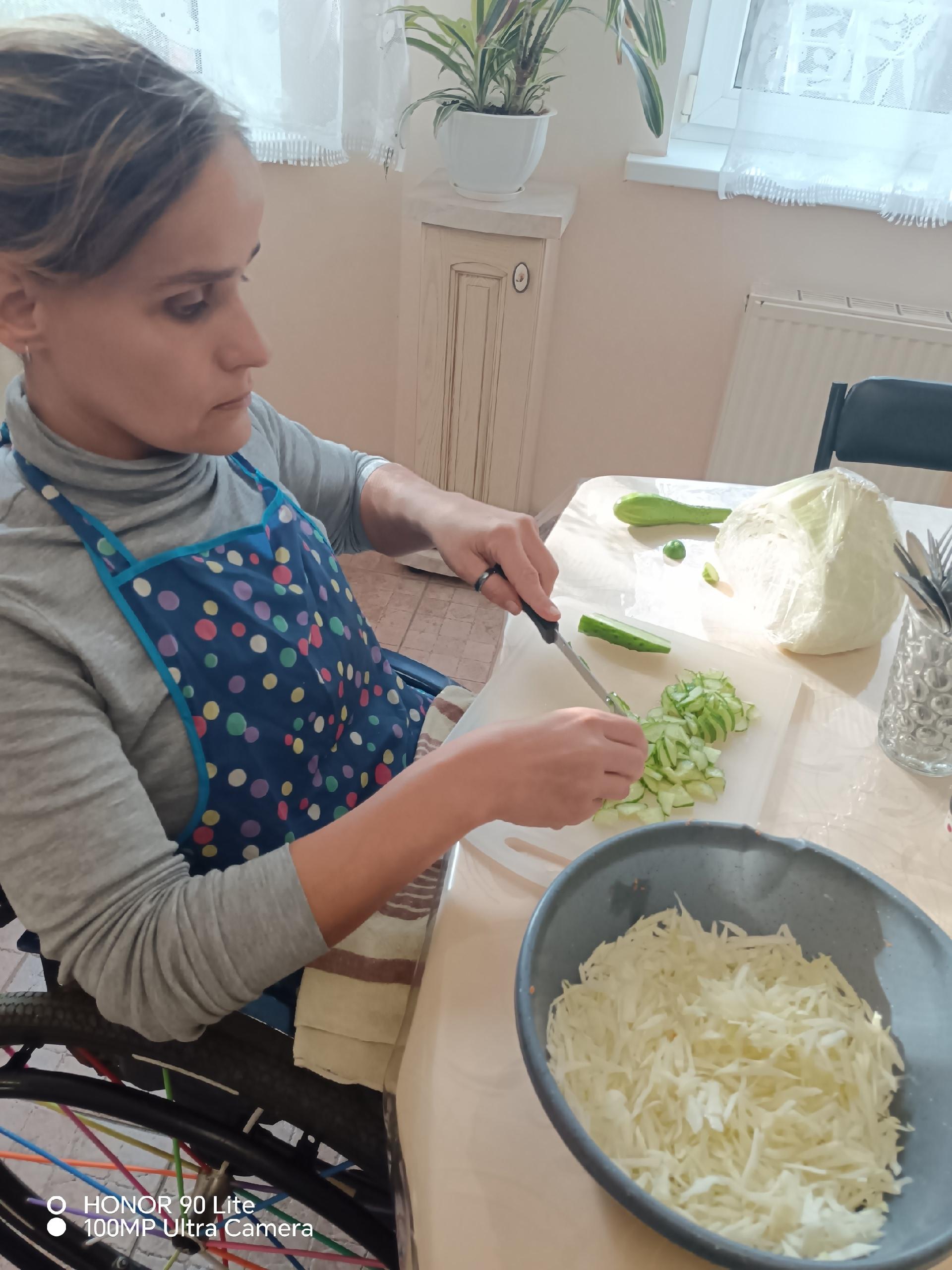 Женщина в фартуке нарезает огурец для салата за столом