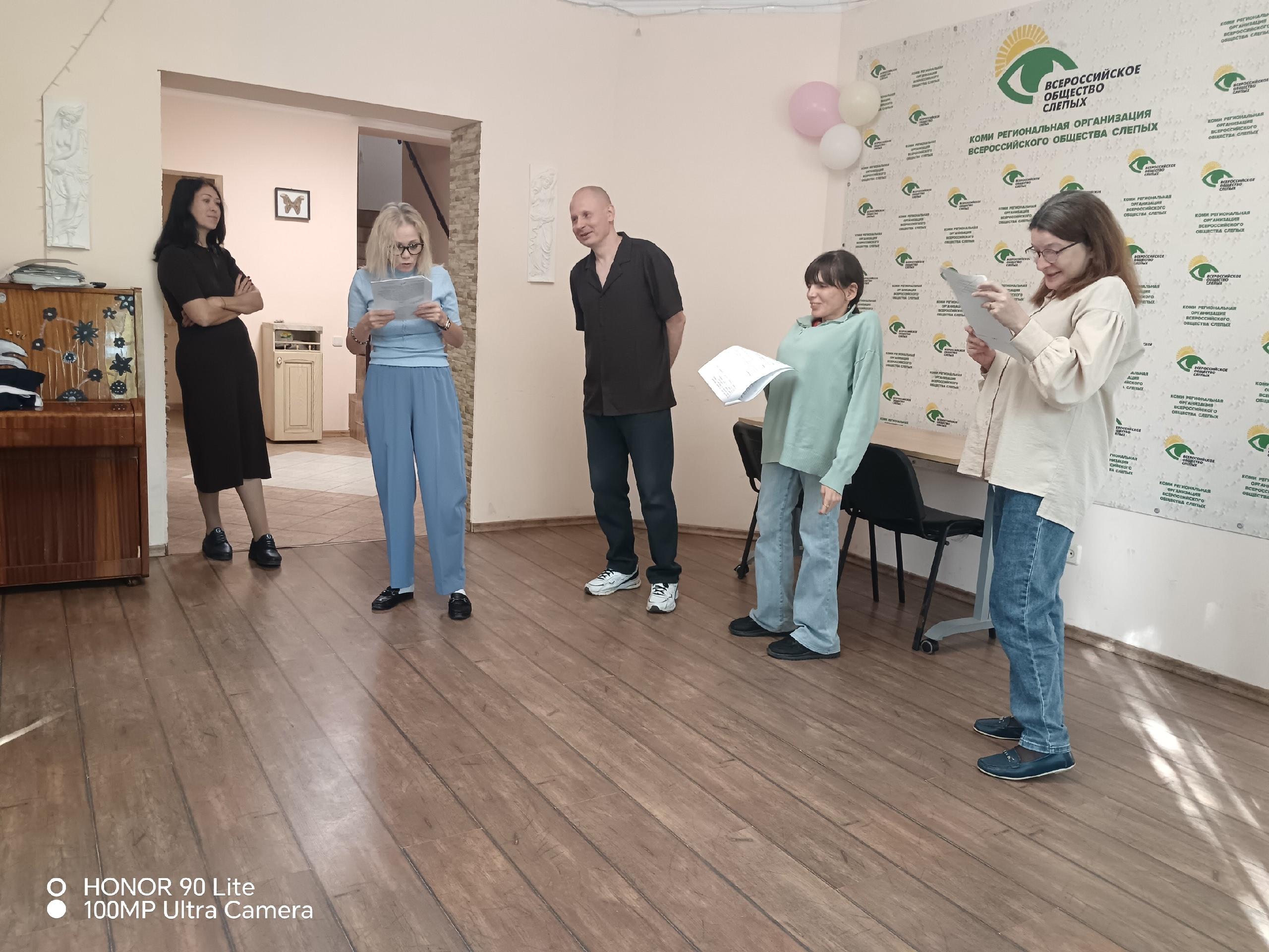 Участники репетиции с листами бумаги в руках стоят в зале