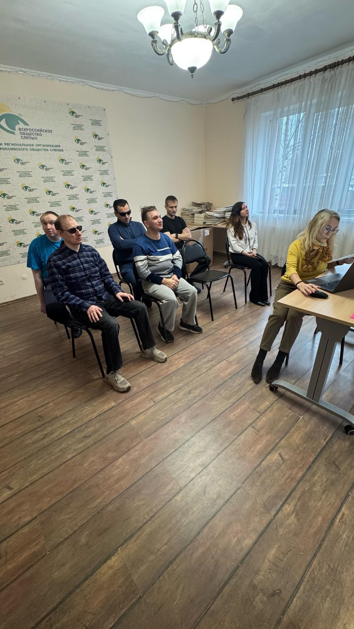Люди сидят на стульях и слушают выступающего за столом