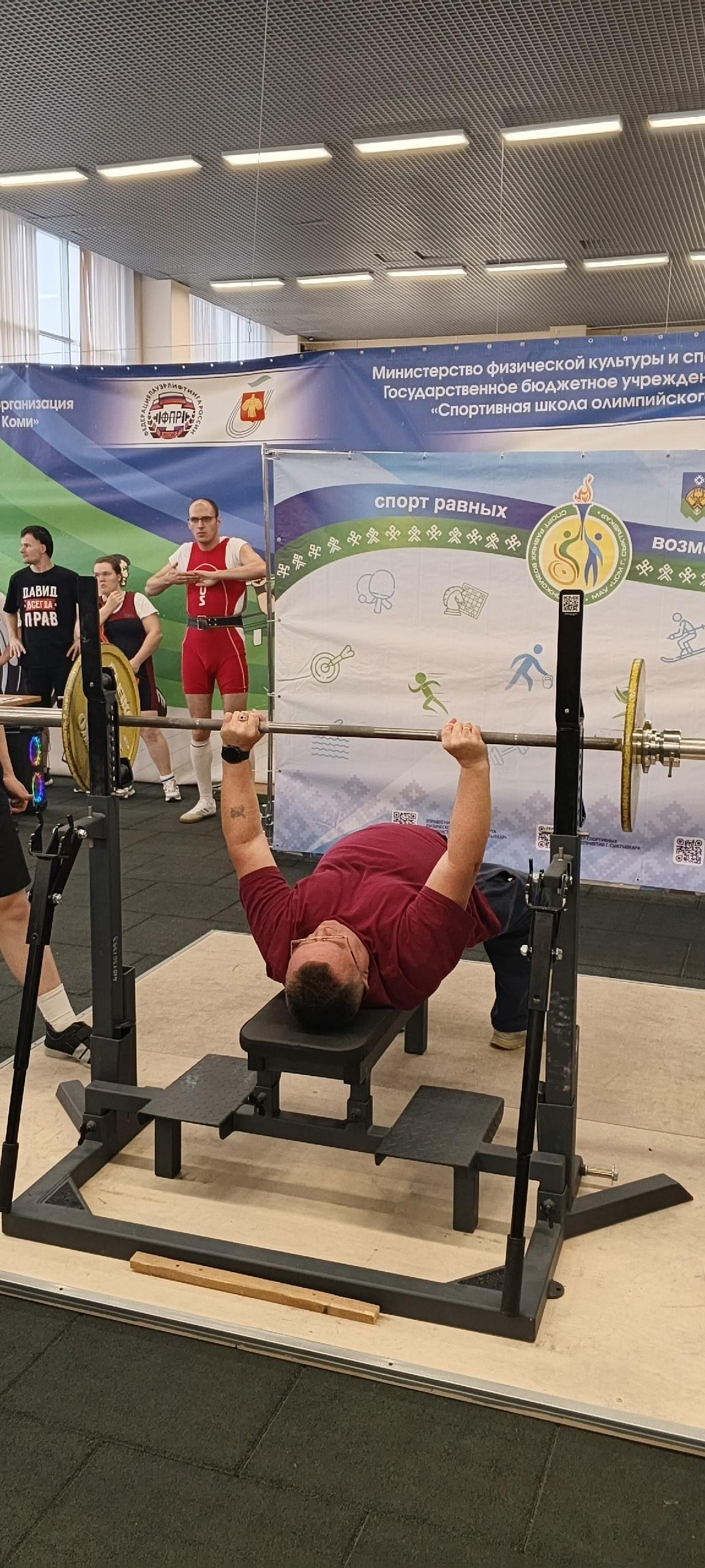 Спортсмен выполняет жим штанги лежа на фоне баннера соревнований
