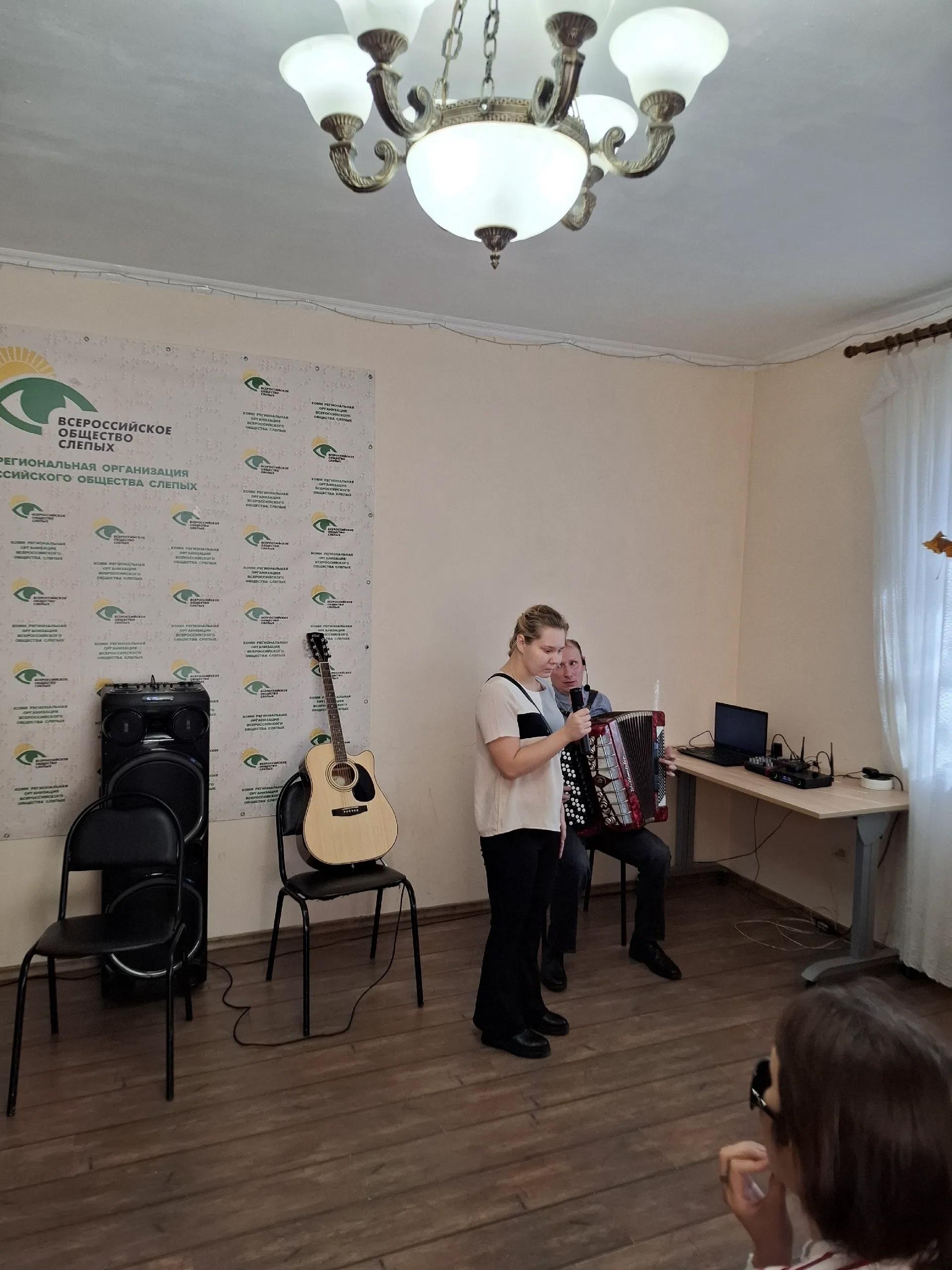 Женщина поет в микрофон рядом с баянистом на сцене