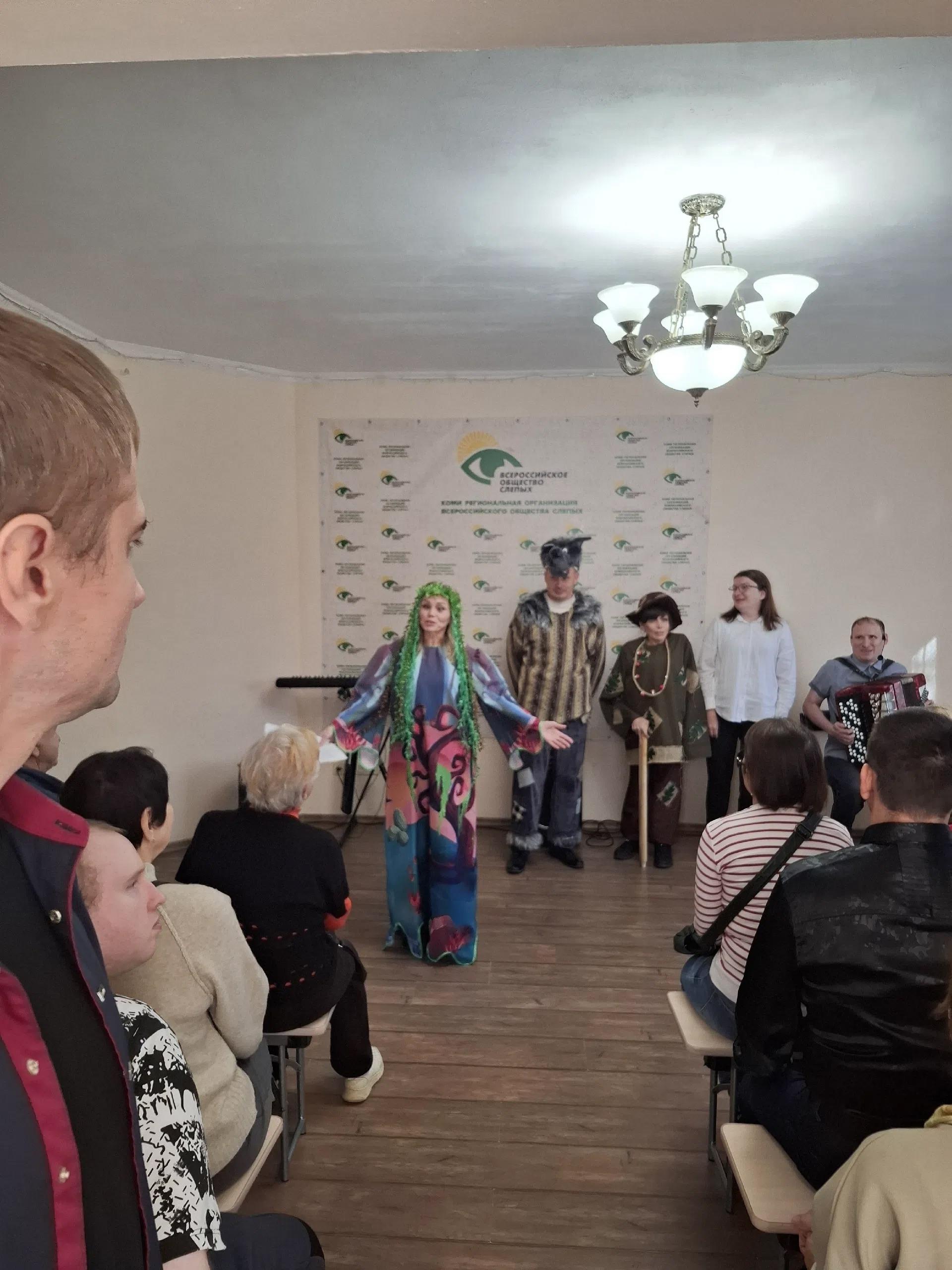Женщина в ярком костюме кикиморы выступает перед зрителями в зале