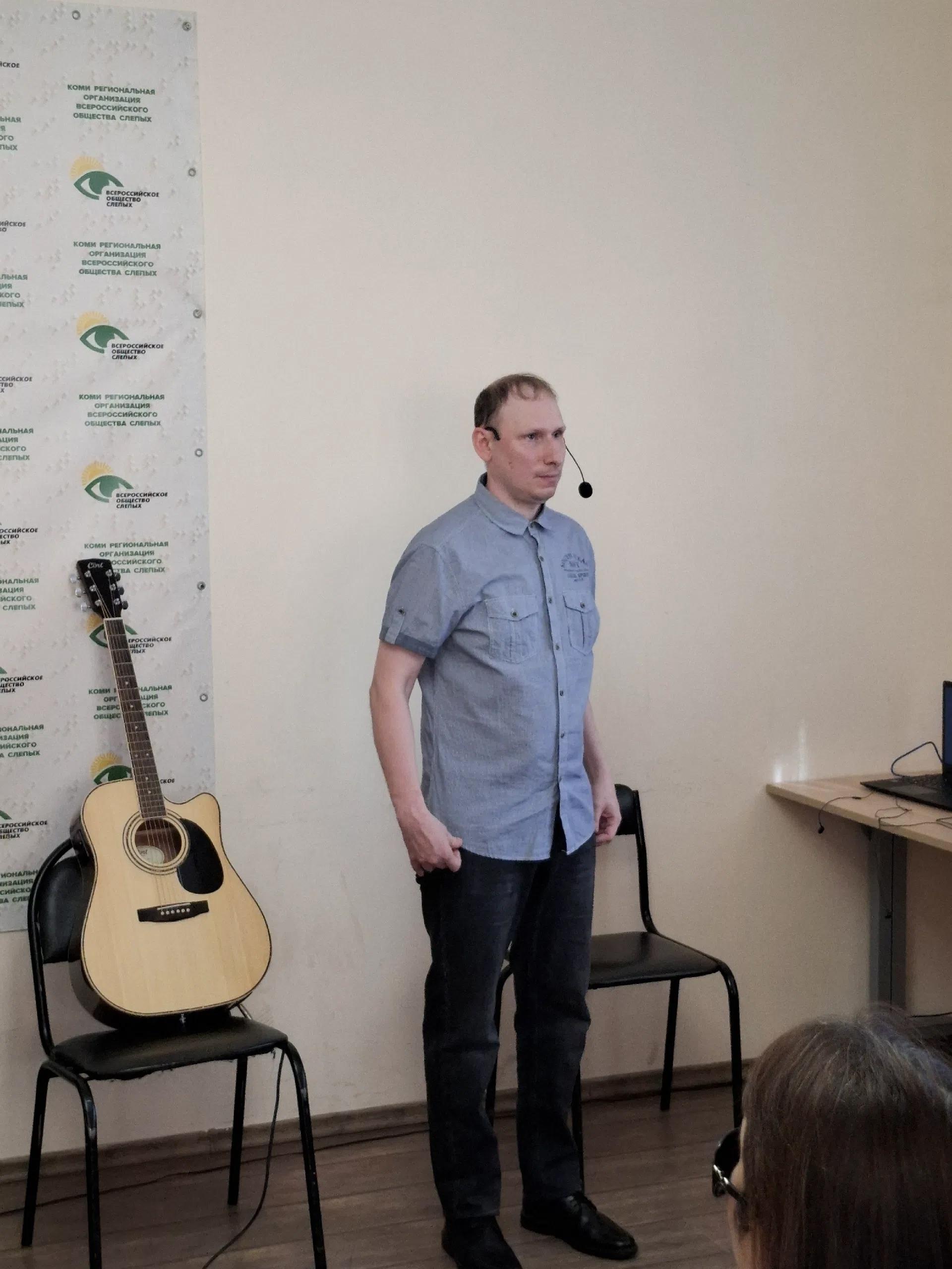 Мужчина в рубашке выступает перед зрителями рядом со студийной гитарой
