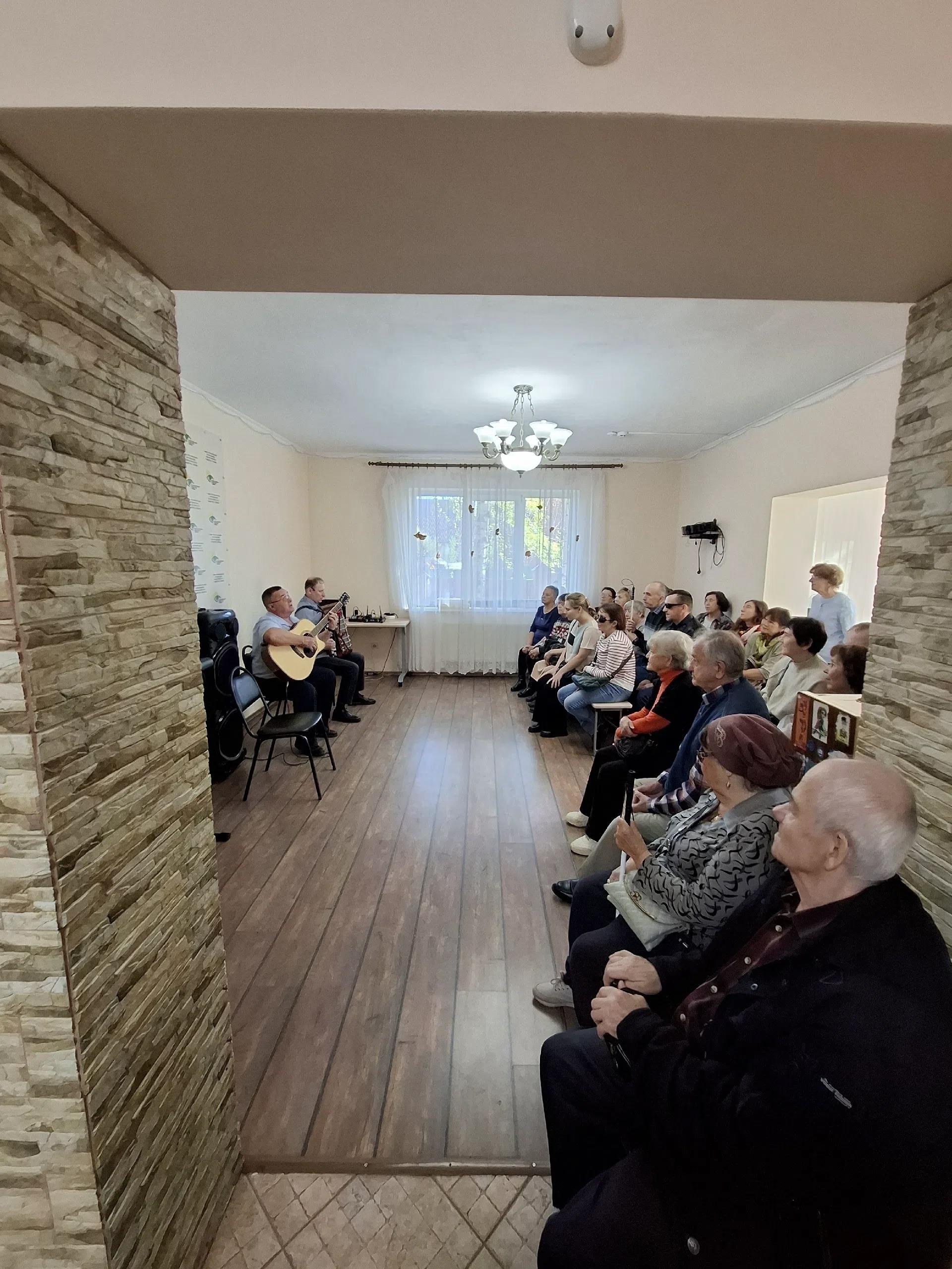 Зрители сидят на скамьях в зале и смотрят выступление музыкантов
